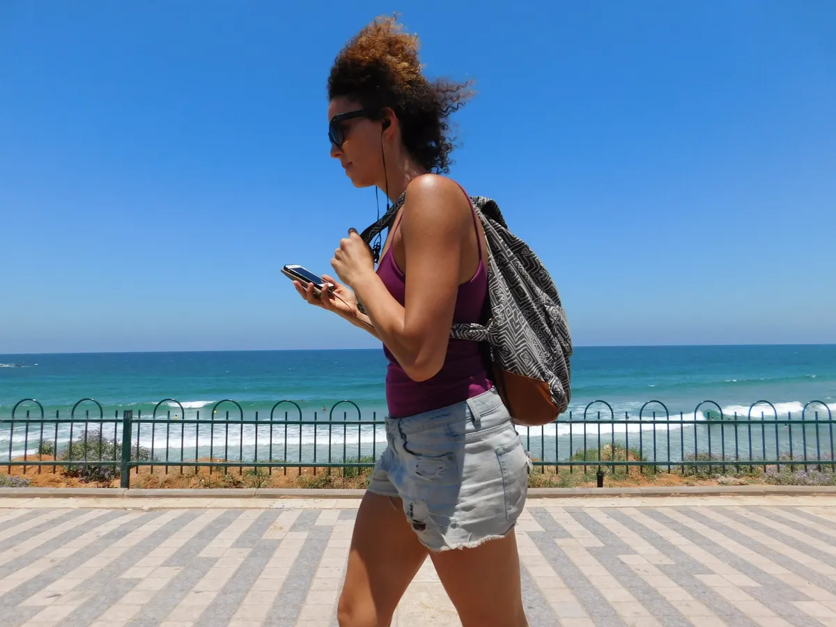 אישה הולכת לאורך חוף תל אביב ביום שמש